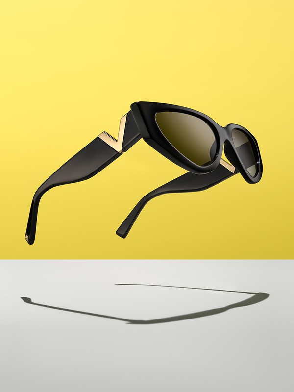 Elevated black sunglasses with gold accents and brown lenses against a vibrant yellow backdrop, casting a distinct shadow.