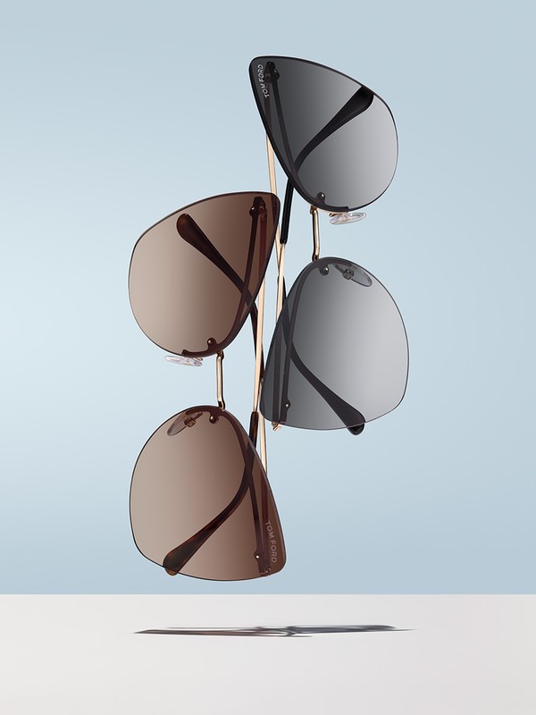 Eye-level studio shot of four Tom Ford sunglasses with silver and brown gradient lenses arranged on a gold metal rack against a pale blue backdrop.