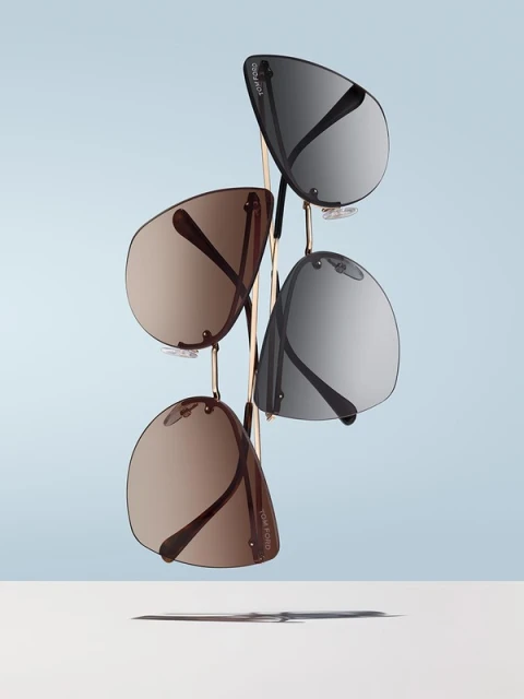 Eye-level studio shot of four Tom Ford sunglasses with silver and brown gradient lenses arranged on a gold metal rack against a pale blue backdrop.
