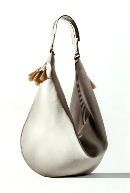 Silver hobo bag with tassels on a white background. Fashionable accessory for women, featuring a soft slouch and metallic finish.