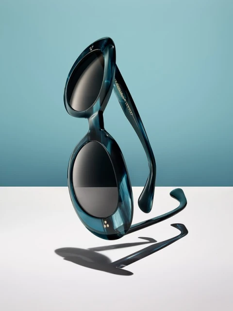 Elegant blue sunglasses, positioned on a white surface against a gradient blue backdrop, creating a captivating studio fashion product shot.