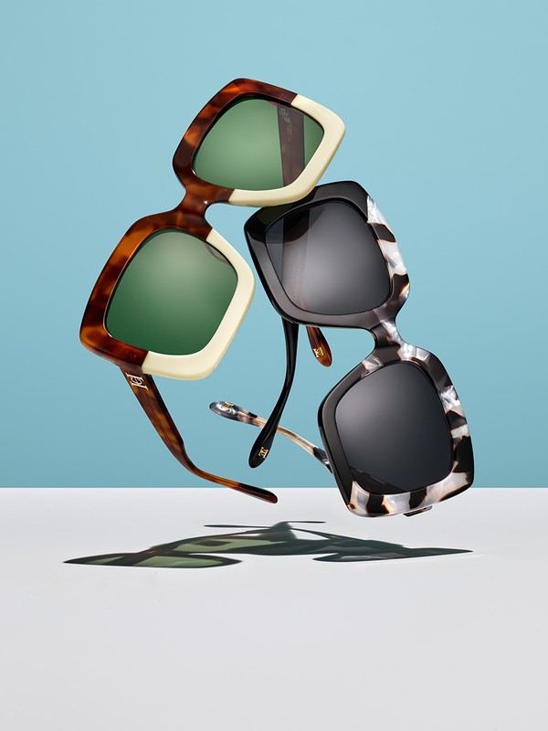 Two pairs of chunky square sunglasses stacked floating against a blue and white background