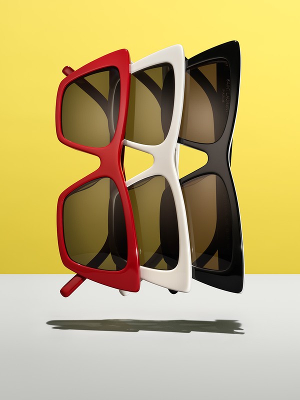 Studio shot of a row of three stylish sunglasses in red, white, and black with a solid yellow background and a subtle shadow.
