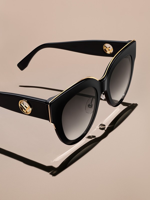 Stylish black Fendi sunglasses featuring gold accents and subtle branding, casting a shadow on a gradient neutral backdrop. Fashion accessory.