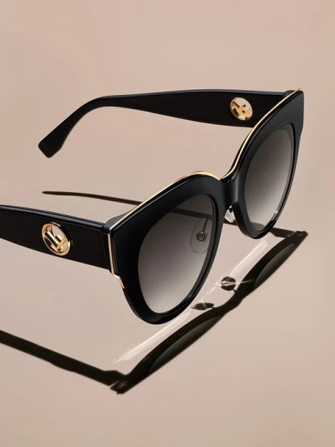 Stylish black Fendi sunglasses featuring gold accents and subtle branding, casting a shadow on a gradient neutral backdrop. Fashion accessory.