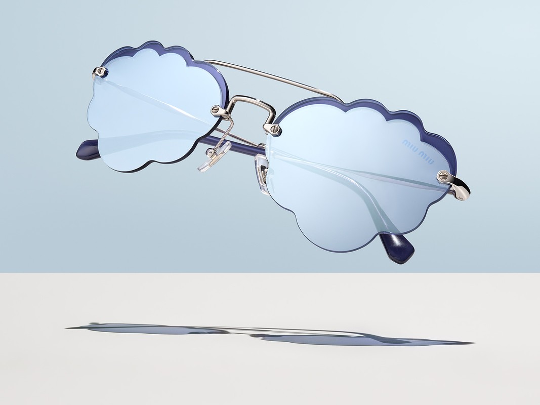 Cloud-shaped Miu Miu sunglasses in light blue with silver metal frames and dark blue rims, casting a shadow on white surface.
