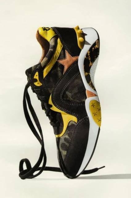 High-angle studio shot of a black sneaker with camouflage pattern and a white sole, resting on a solid light surface.