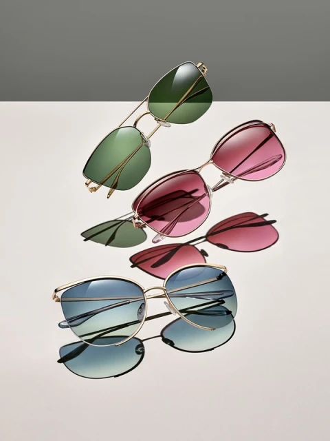 Still life studio shot featuring three pairs of gold-framed sunglasses with green, red, and blue gradient lenses, positioned on a gradient backdrop.