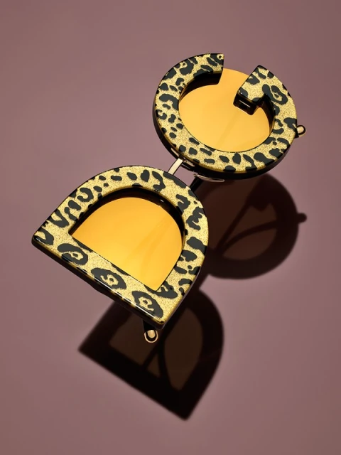 Elevated view of leopard print sunglasses featuring gold lenses, against a solid pink backdrop with shadow.