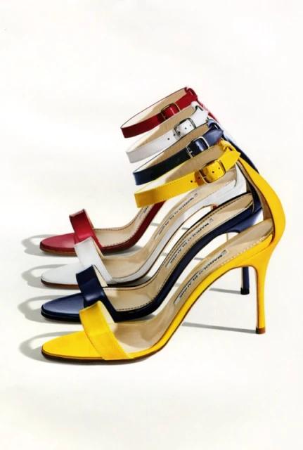 Fashionable red, white, blue and yellow Manolo Blahnik sandals with ankle straps are neatly arranged against a white backdrop.