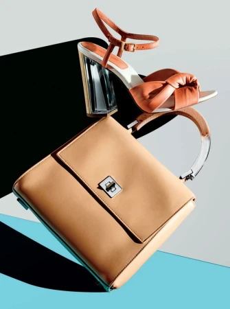Tan leather handbag and coral colored heeled sandal on a turquoise and grey background, studio product photography.