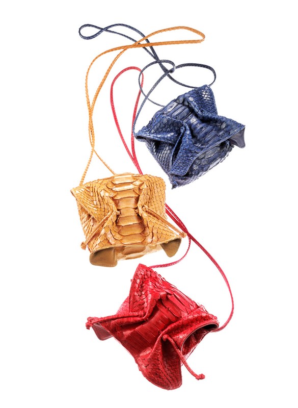 Three reptile leather drawstring pouches in red, tan, and blue, with thin braided straps on a white background. Fashion accessory.