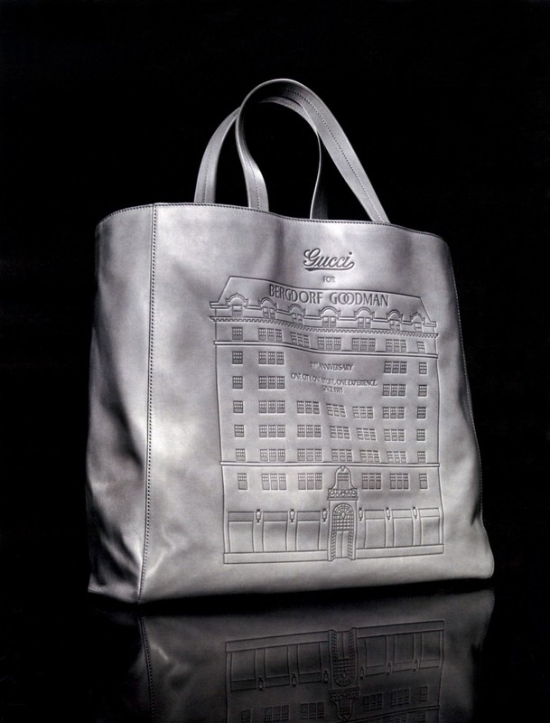 Gucci leather tote bag featuring an embossed building design against a dark background. The bag has top handles and a reflective surface.
