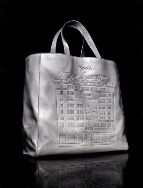 Gucci leather tote bag featuring an embossed building design against a dark background. The bag has top handles and a reflective surface.