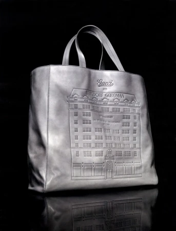 Gucci leather tote bag featuring an embossed building design against a dark background. The bag has top handles and a reflective surface.
