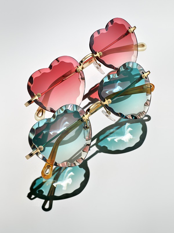 Heart-shaped sunglasses in red and blue, casting shadows on a white background, fashion eyewear with a playful design.