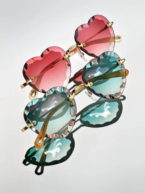 Heart-shaped sunglasses in red and blue, casting shadows on a white background, fashion eyewear with a playful design.