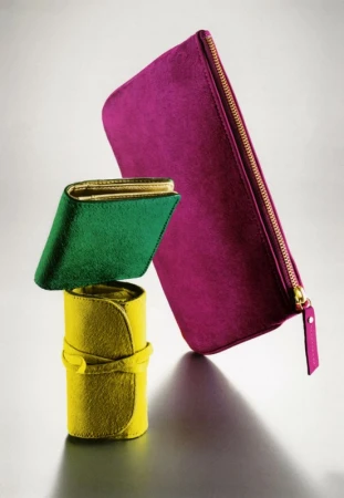 Elevated still life featuring a yellow rolled case, a green wallet, and a fuchsia zippered case against a gradient gray background.
