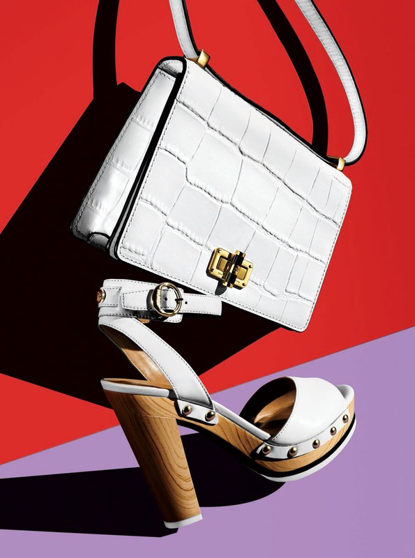 Fashion still life of a white crocodile-skin handbag and a white sandal with a wooden heel against a vibrant red and purple backdrop.