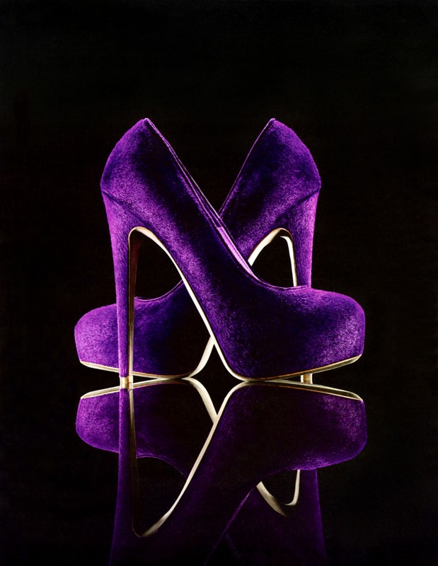 Two purple velvet high heel shoes are displayed on a reflective black surface against a dark background. Fashion, footwear, and luxury concept.
