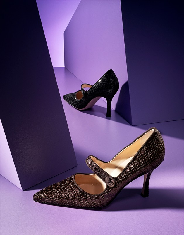 Two high-heeled Mary Jane shoes in brown and black, are displayed against a geometric purple background in a studio product shot.