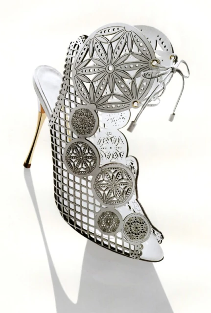 High-heel shoe, crafted from white leather with intricate metalwork and a stiletto heel, elegantly displayed on a clean white background.