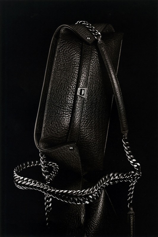 Studio shot of a black leather tote bag with a chunky silver chain strap, showcasing its texture and design against a dark backdrop.