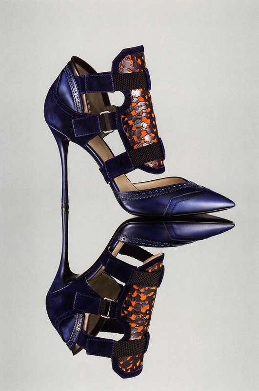 Stylish navy blue high-heeled pump with strappy design and snakeskin-patterned embellishments, presented on a reflective surface.