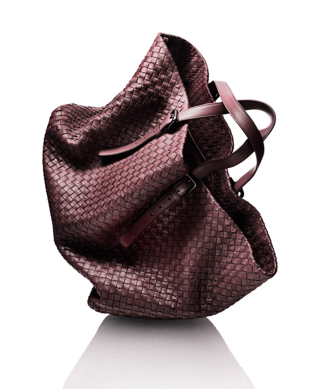 Studio shot of a brown woven leather hobo bag with brown leather handles against a white background with a subtle reflection.