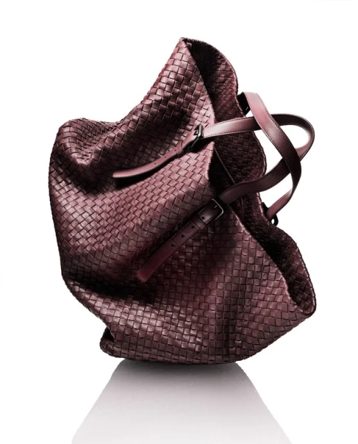 Studio shot of a brown woven leather hobo bag with brown leather handles against a white background with a subtle reflection.