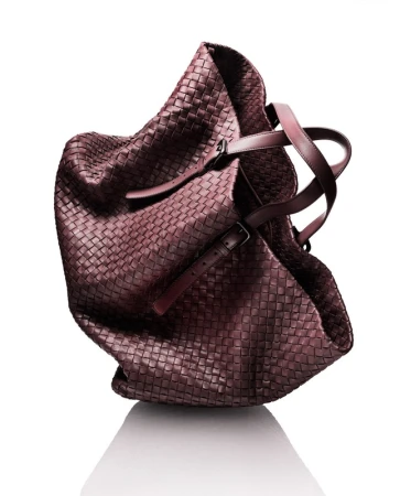 Studio shot of a brown woven leather hobo bag with brown leather handles against a white background with a subtle reflection.
