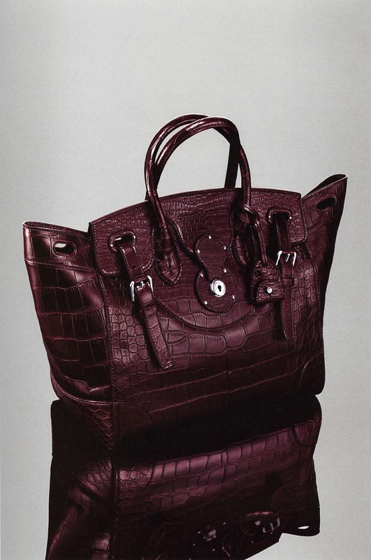 Burgundy crocodile-patterned leather satchel handbag with silver hardware, set against a neutral grey background and reflective surface.