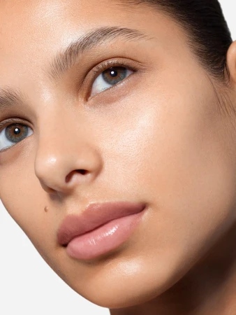 Close up beauty portrait of a woman face with natural makeup and glossy lips against a neutral background