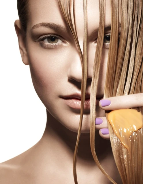 Close-up studio shot of a fair-skinned woman with wet blonde hair partially covering her face, hand applying hair product.