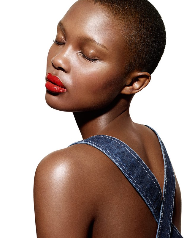 Glamour shot of an adult female with closed eyes and red lipstick wearing denim straps in a studio with a white background.