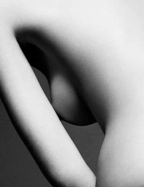 Monochromatic photograph featuring the side of a woman's body with her arm raised, showcasing skin texture and a minimalist aesthetic.