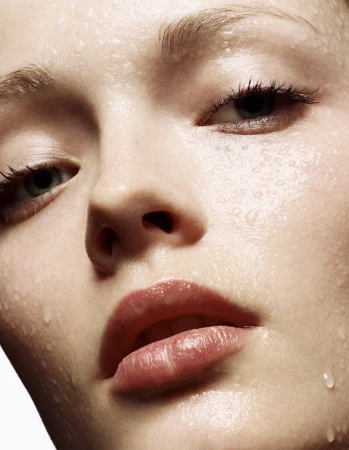 Close-up beauty portrait of a woman's face covered in water droplets with a neutral expression