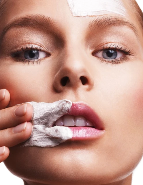 Close-up portrait of an adult female applying a white facial mask. Focus on skincare, beauty treatment, and healthy complexion.