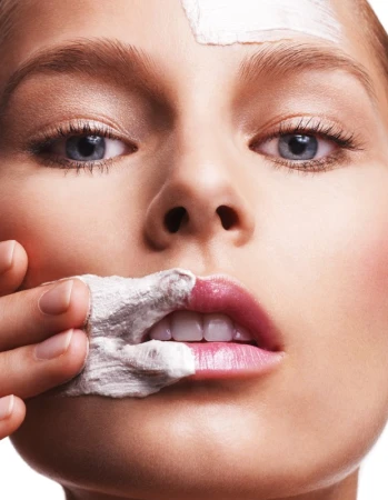 Close-up portrait of an adult female applying a white facial mask. Focus on skincare, beauty treatment, and healthy complexion.