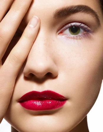 Close up beauty portrait of a woman with vibrant red lipstick and a hand partially covering her face shot by Philippe Salomon