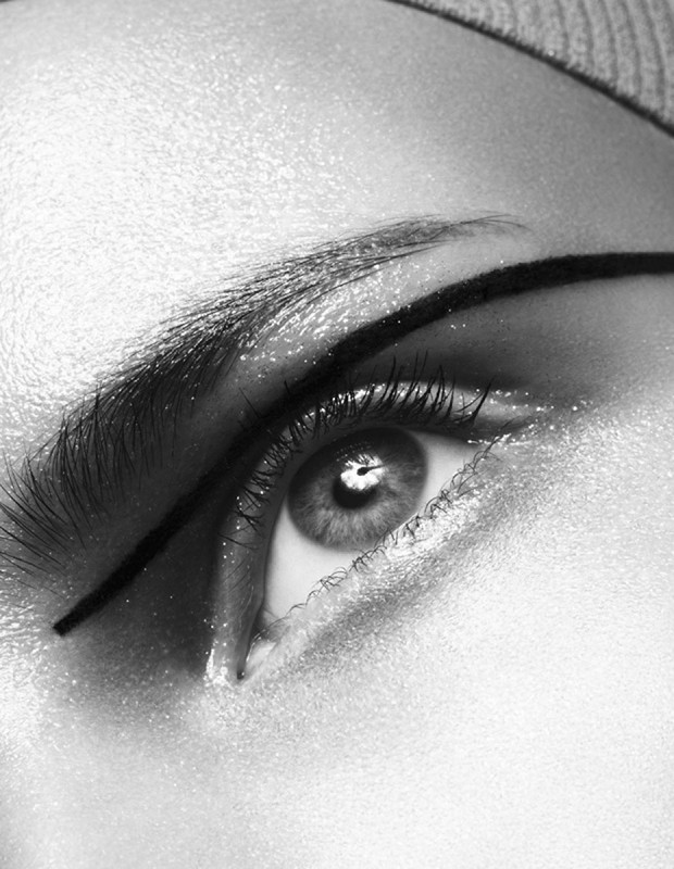 Close-up black and white shot of a woman's eye with heavy eyeliner, brow, and sparkly skin.