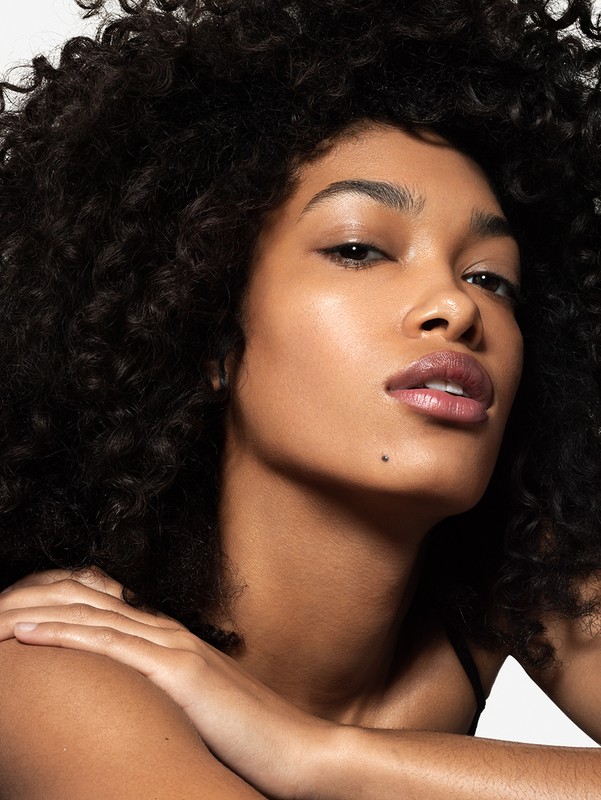 Close-up portrait of an adult woman with dark curly hair posing with her arms crossed in a photo studio setting.