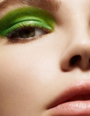 Extreme close-up portrait of a woman with vibrant metallic green eyeshadow and glossy nude lips.
