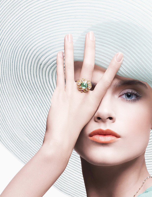 Close-up of a light-skinned adult female wearing a wide-brimmed hat and a ring, covering her face with her hand in a studio.