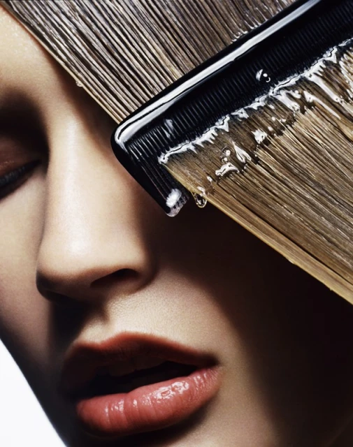 Close-up of a woman's face with wet hair being combed; the comb and hair have droplets of water, creating a sleek and clean beauty shot.