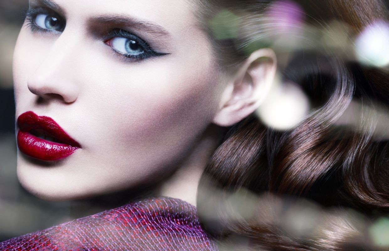 Close-up beauty portrait of a woman with dramatic winged eyeliner, glossy red lips, and dark brown hair, photographed by Philippe Salomon.