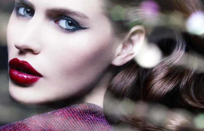 Close-up beauty portrait of a woman with dramatic winged eyeliner, glossy red lips, and dark brown hair, photographed by Philippe Salomon.