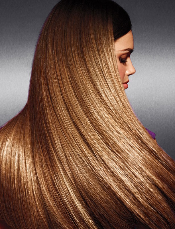 Profile view of a woman with long, straight, shiny brown hair cascading down her back against a dark gray background in a beauty shot.