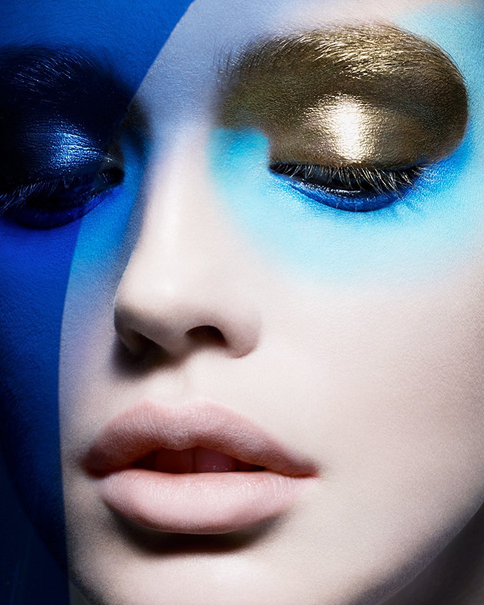 Close-up portrait of a woman with vibrant blue eyeshadow and a metallic gold accent across her eyelid.