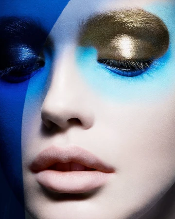 Close-up portrait of a woman with vibrant blue eyeshadow and a metallic gold accent across her eyelid.